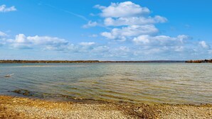 A clear view of a lake with a pebbly shore and distant land. - Lakefront 4BR w/ Stunning Views, Dock & Porch (Auburn)