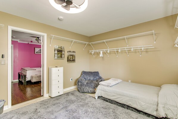 A bedroom with a bed, a dresser, a hanging clothes rack, and a door leading to another room.