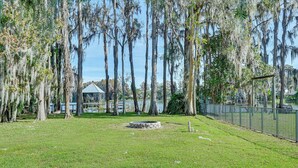 A park with a grassy area, trees with Spanish moss, a small pond, and a metal fence. - Dock, Lanai & Pool! Modern Red Bug Lake Retreat (Land O' Lakes)