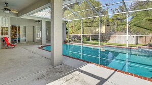 A covered swimming pool with a glass enclosure, red lounge chairs, and a ceiling fan. - Dock, Lanai & Pool! Modern Red Bug Lake Retreat (Land O' Lakes)