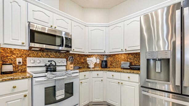 A modern kitchen with white cabinets, stainless steel appliances, and granite countertops. - Dock, Lanai & Pool! Modern Red Bug Lake Retreat (Land O' Lakes)