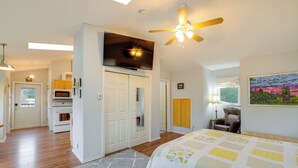 A bedroom with a bed, a ceiling fan, a TV, and a kitchen area with a microwave and oven. - Olympic Mtn Views! Cozy Carriage House in Sequim (Sequim)