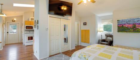 A bedroom with a bed, a ceiling fan, a TV, and a kitchen area with a microwave and oven.