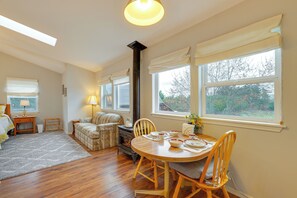 A cozy living room with a fireplace, a dining table with chairs, a sofa, and a window with curtains. - Olympic Mtn Views! Cozy Carriage House in Sequim (Sequim)