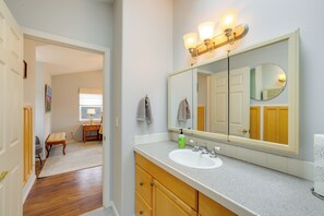A bathroom with a large mirror, a sink, and a vanity. There is a bench in the adjacent room. - Olympic Mtn Views! Cozy Carriage House in Sequim (Sequim)