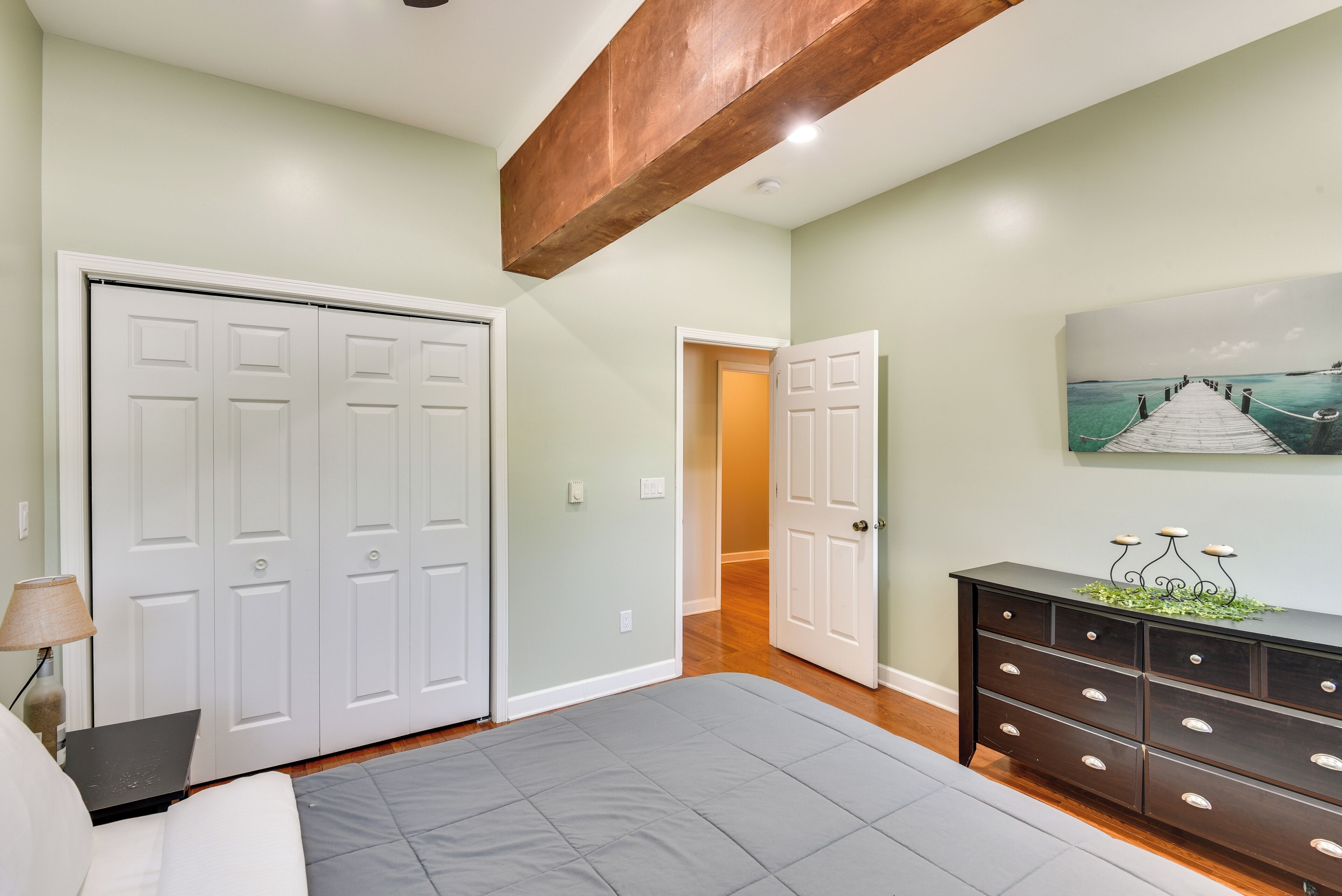 A bedroom with a bed, a dresser, and a door leading to another room.