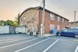 A parking lot with a blue car, a brick building with a garage, and utility equipment. - Cozy Sawyer Apartment - 2 Mi to Warren Dunes Park! (Sawyer)