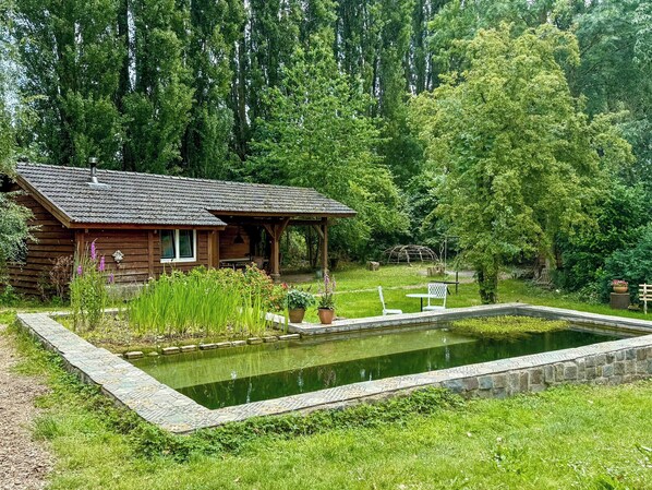 En rustik hytte med en sø, omgivet af frodig vegetation og høje træer.