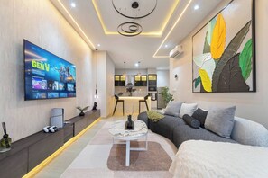 A modern living room with a flat-screen TV, a sofa, a coffee table, and a dining area in the background. - Chic Waterfront 2BR in Lekki Phase 1 - 5 Star Apt (Lekki)