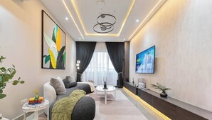 A modern living room with a sofa, a coffee table, and a TV mounted on the wall. - Chic Waterfront 2BR in Lekki Phase 1 - 5 Star Apt (Lekki)