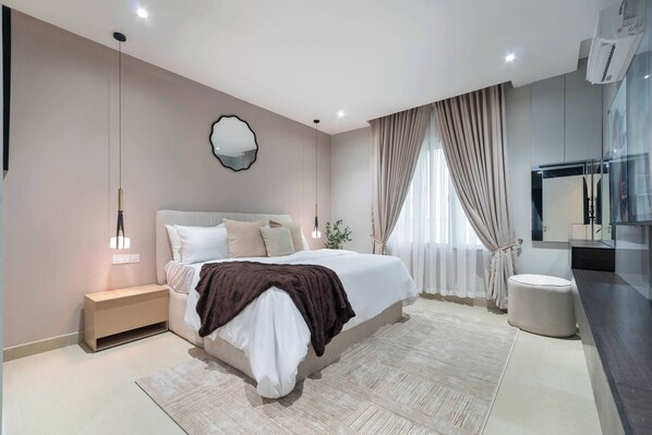 A modern bedroom with a large bed, bedside tables, a mirror, and a built-in TV. - Chic Waterfront 2BR in Lekki Phase 1 - 5 Star Apt (Lekki)
