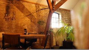 A rustic room with exposed brick walls, a wooden ceiling, and a round table with chairs. There are potted plants and a window with natural light. - Grutte Brekken Tuinkamer (Weidum)