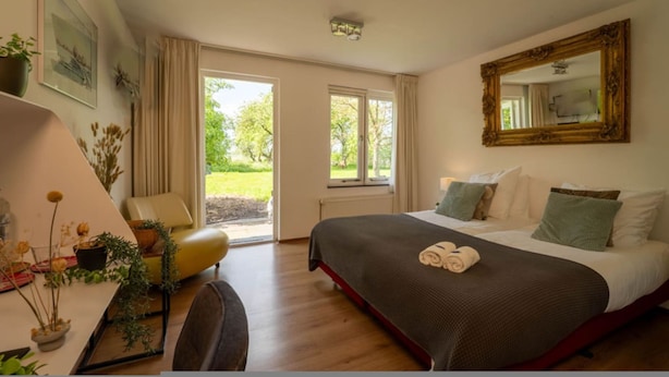 A hotel room with a bed, a desk, a chair, a large window, and a mirror. - Grutte Brekken Tuinkamer (Weidum)