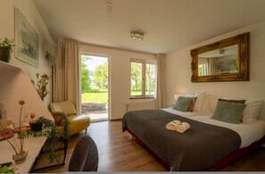 A hotel room with a bed, a desk, a chair, a large window, and a mirror. - Grutte Brekken Tuinkamer (Weidum)