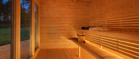 A wooden sauna with benches and a bench seat, a wooden floor, and a glass door.
