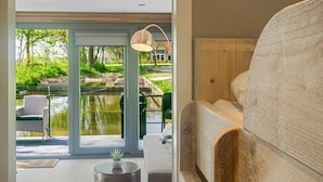 A modern bedroom with a wooden headboard, a large window, and a view of a pond outside. - Fokke Sleat Houseboat (Weidum)