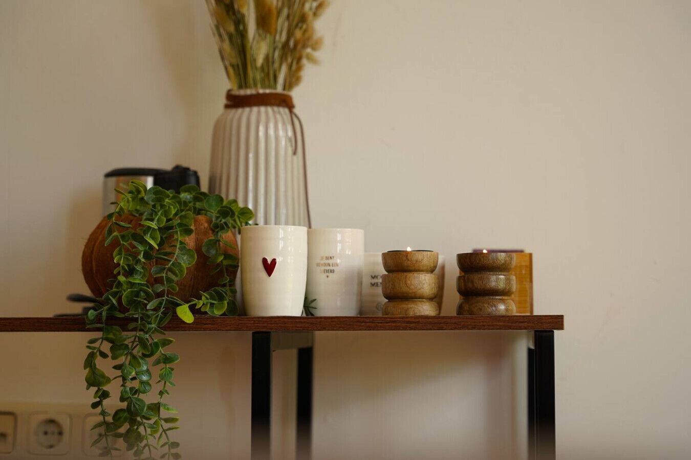 A wooden shelf with a potted plant, a vase with dried flowers, and three candle holders.