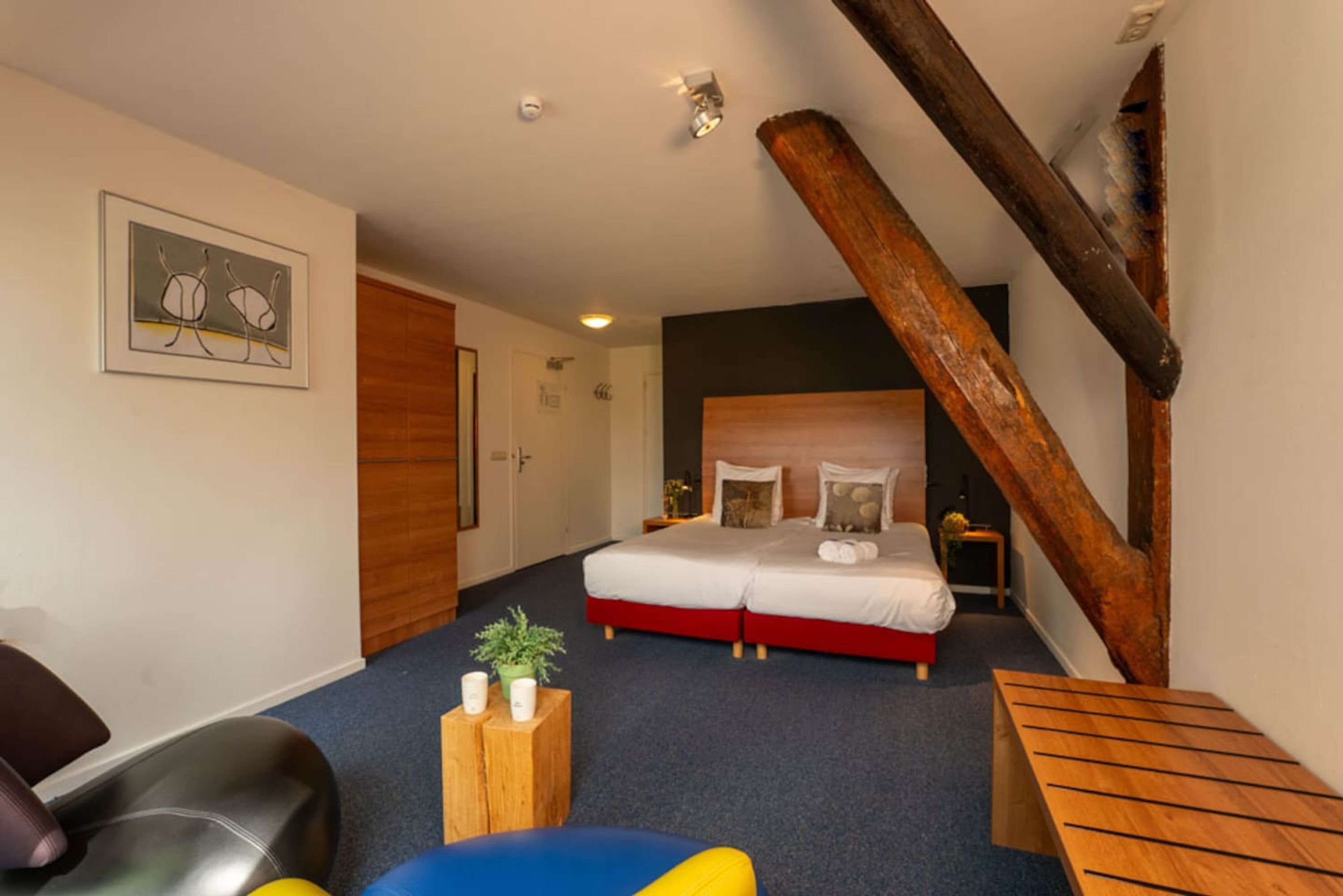 A bedroom with a large bed, wooden beams, a desk, and a chair.