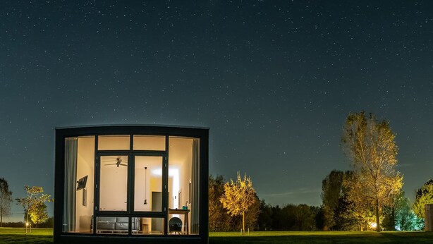 A modern, glass-walled structure with a ceiling fan, a bed, and a desk, set against a night sky with stars. - Anjewiel Weidesuite in Weidum (Weidum)