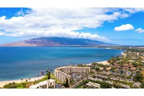 A coastal resort with a large building, beachfront, and a mountain in the background. - Sweeping Ocean Views & Elegant Interior - Menehune Shores #308 Oceanfront Condo (Kihei, Maui)