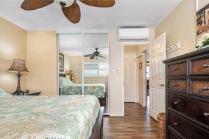 A bedroom with a bed, a ceiling fan, an air conditioning unit, a dresser, and a hallway leading to another room. - Sweeping Ocean Views & Elegant Interior - Menehune Shores #308 Oceanfront Condo (Kihei, Maui)