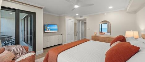 A bedroom with a large bed, a ceiling fan, a TV on the wall, and a sliding glass door leading to a balcony.
