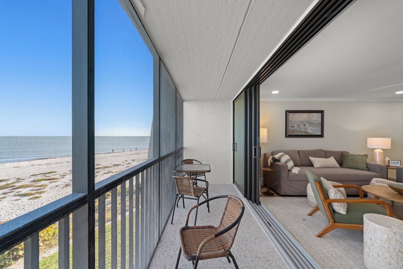 Un balcon avec vue sur la plage, un coin repas avec des chaises en osier et un salon avec un canapé et des lampes.