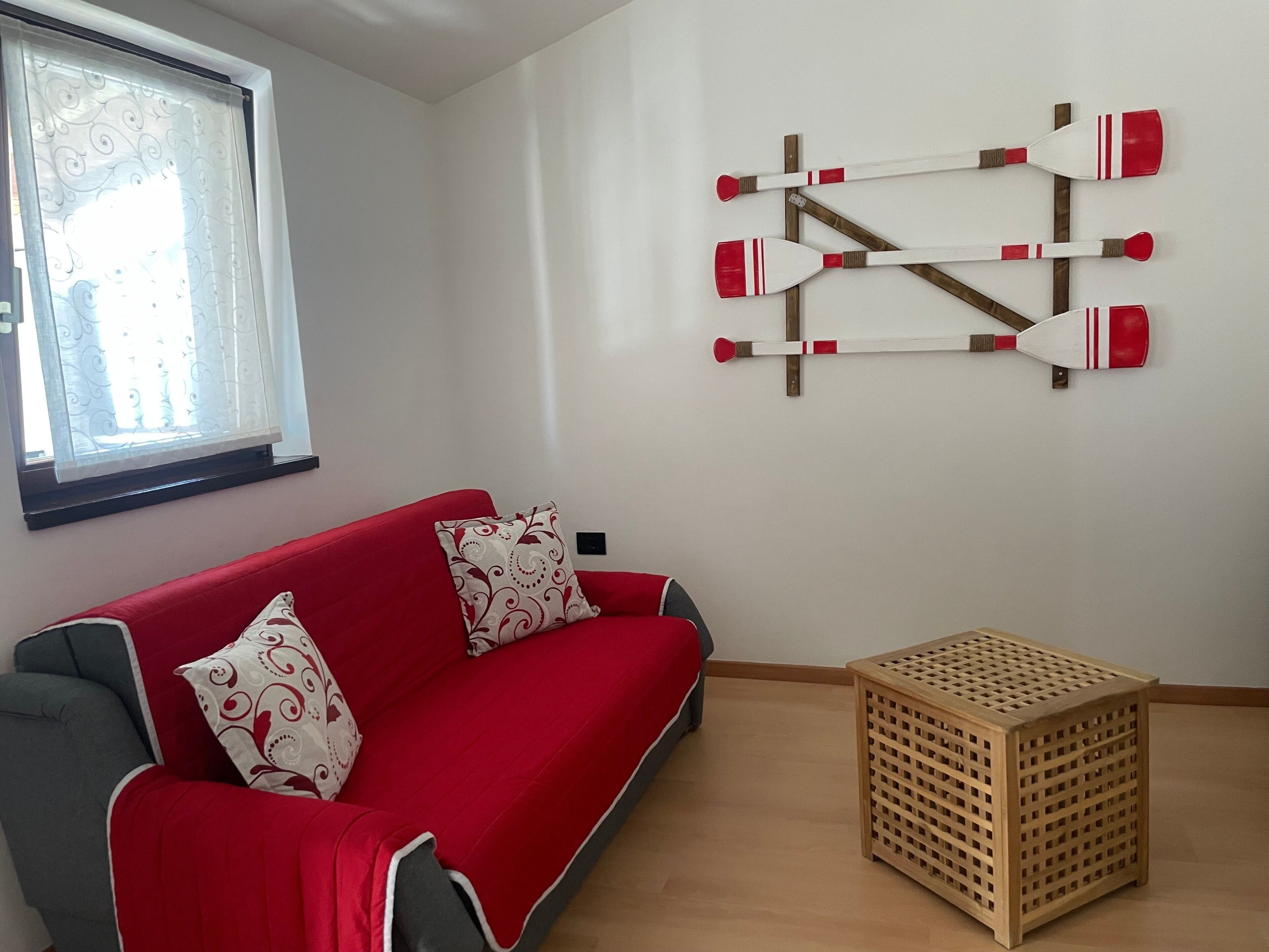 A room with a red sofa, patterned cushions, a wooden crate, and a wall-mounted paddleboard rack.