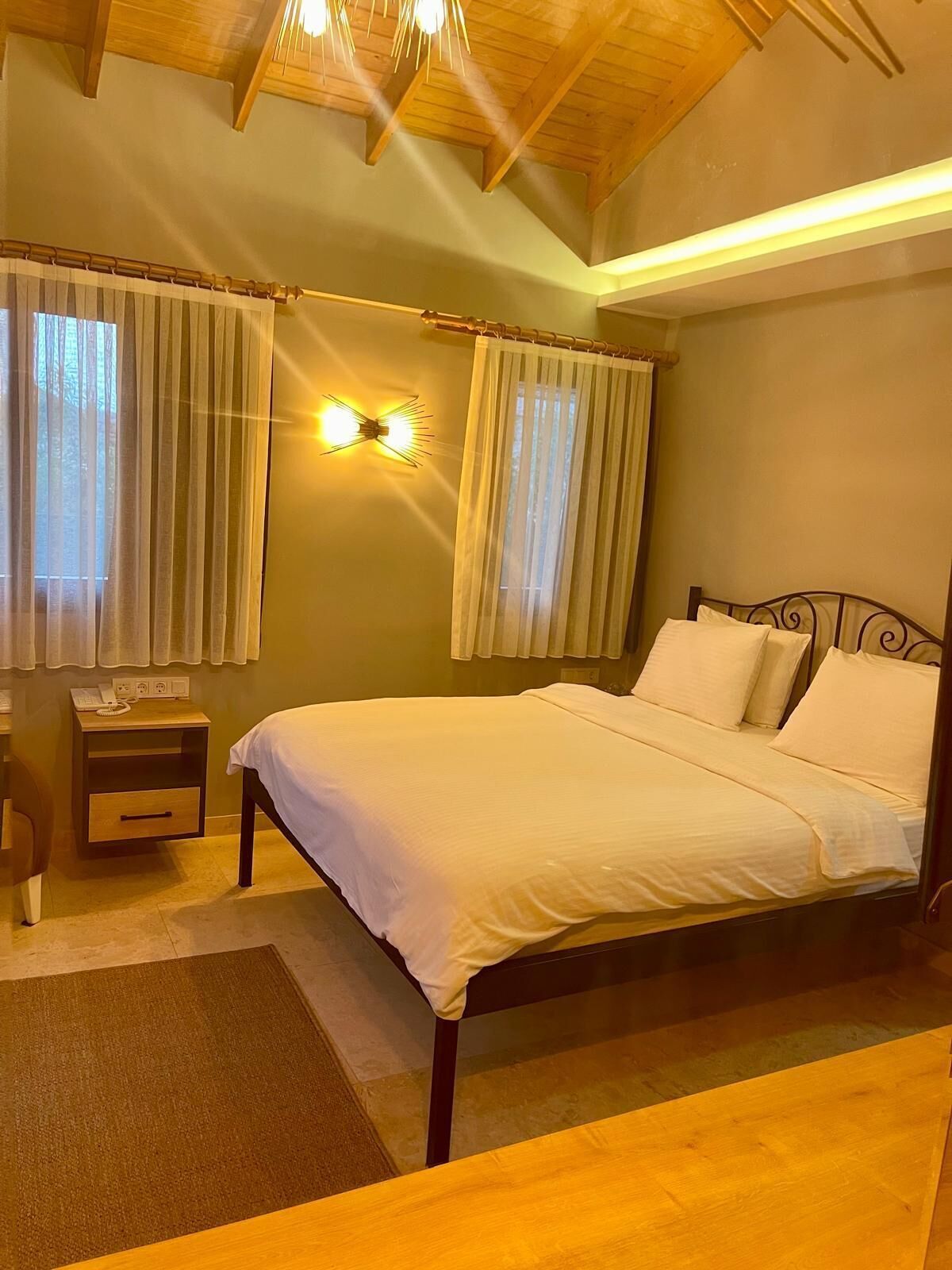 Un dormitorio con una cama de madera, dos mesitas de noche y una lámpara fijada a la pared.