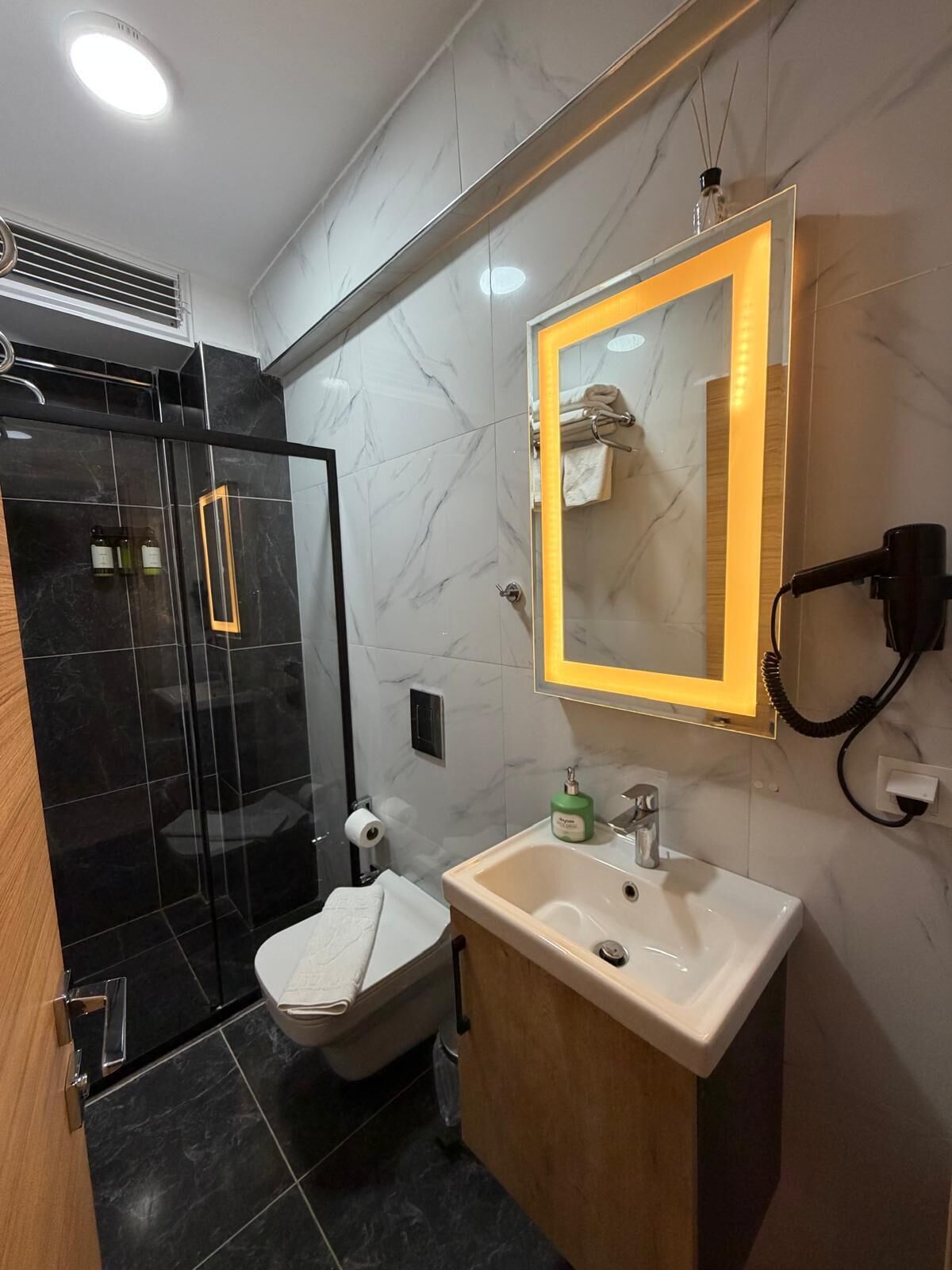 Une salle de bain moderne avec une douche à parois de verre, un lavabo blanc et un miroir avec un cadre jaune.