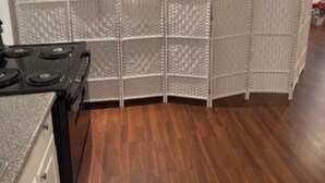 A kitchen with a black stove, wooden flooring, and a white partition with a textured pattern.