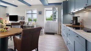 Une cuisine moderne avec des meubles blancs, une table à manger en bois et un téléviseur à écran plat.