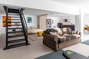 A modern living space with a staircase, a sofa, a small table, and a kitchen area. - Loft apartment with pool, sea and Barcelona views (Teià)