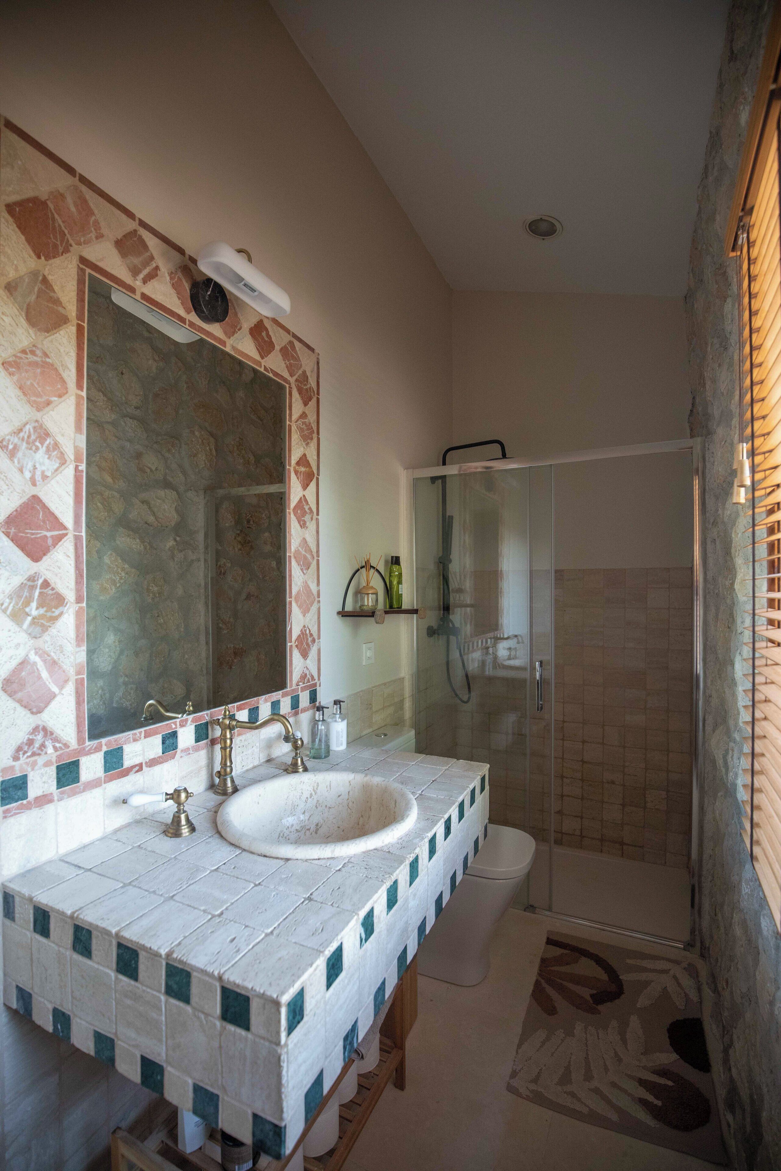 A bathroom with a tiled sink, a large mirror, and a shower.