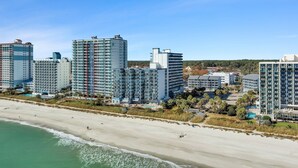 A beachfront hotel with multiple high-rise buildings, a sandy beach, and a clear blue sky. - Salt Air Style- 2 BR Balcony Retreat (Myrtle Beach)