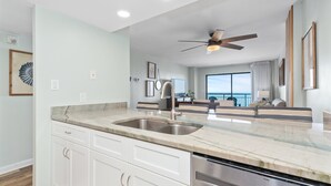 A modern kitchen with a marble countertop, stainless steel sink, and white cabinetry. - Salt Air Style- 2 BR Balcony Retreat (Myrtle Beach)