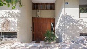A building entrance with a wooden door, a small potted plant, and a stone-paved area.