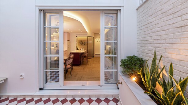 A modern interior with a dining area, kitchen, and a large sliding glass door leading to a balcony with plants.