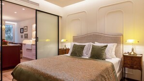A bedroom with a large bed, bedside tables, a sliding door leading to a bathroom, and a view of the outside.