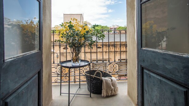 A balcony with a metal railing, a round table with a vase of flowers, and a woven basket with a blanket. - BBarcelona Sants Flat (Barcelona)