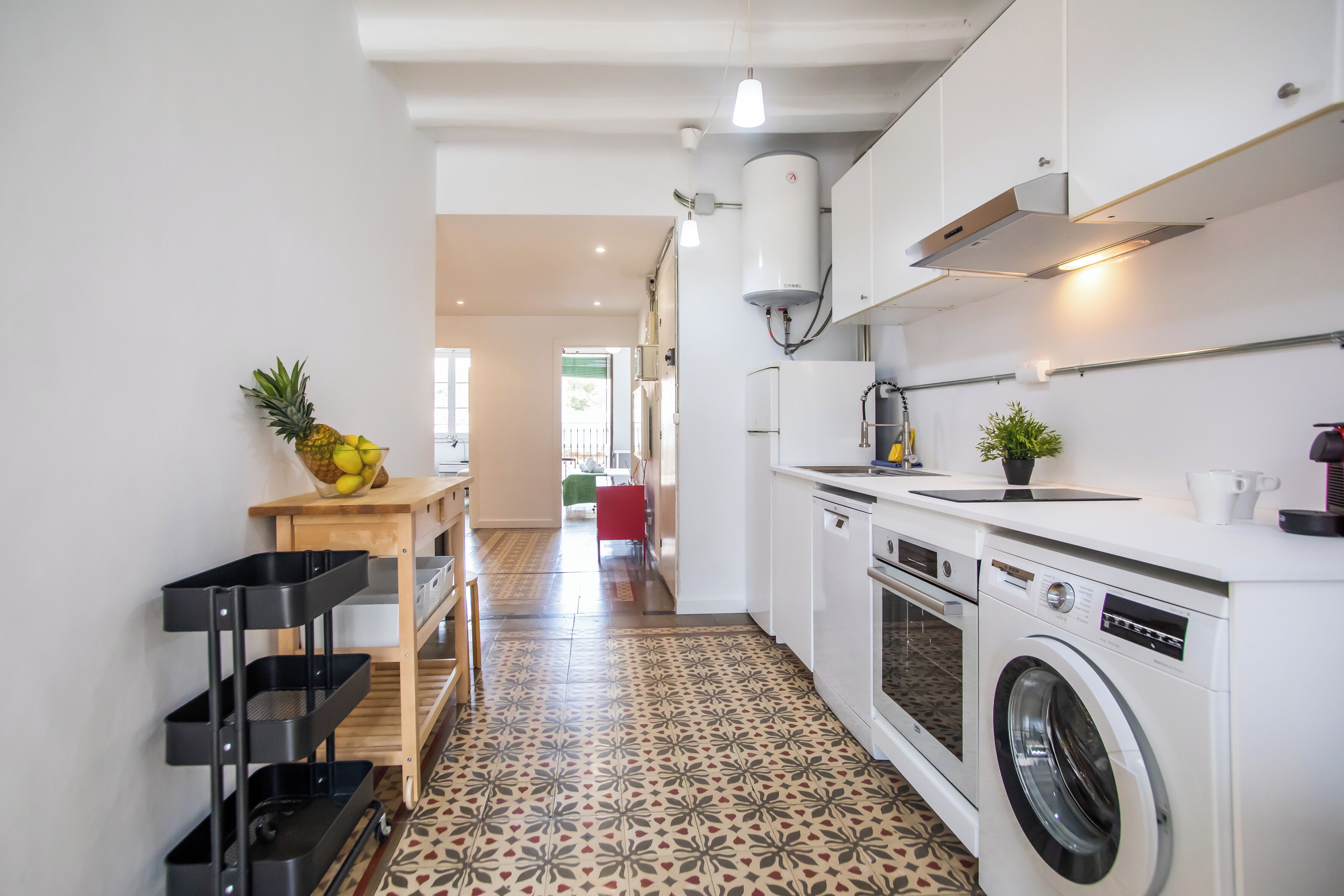 Una cocina moderna con lavadora, una mesa de madera con frutero y piso estampado.