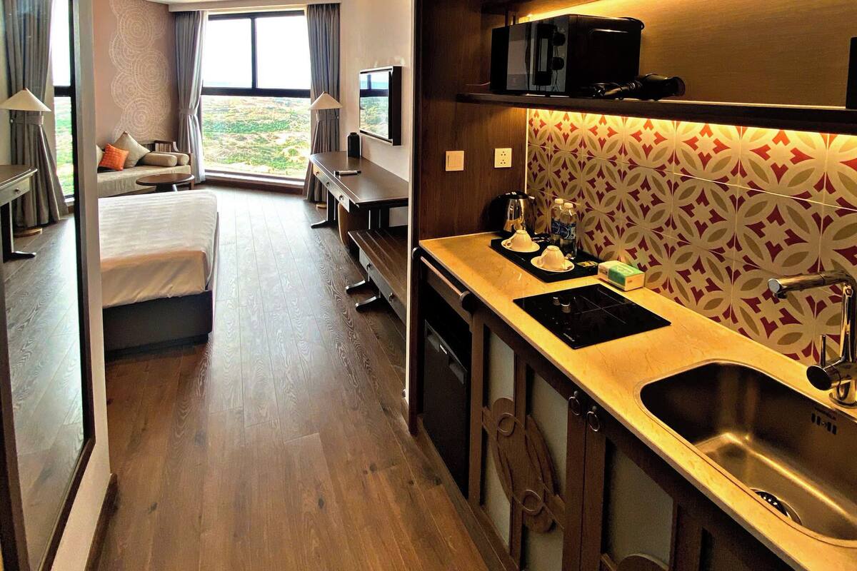 Camera d'albergo compatta con angolo cottura, un letto, una zona salotto con vista e un'ampia finestra.
