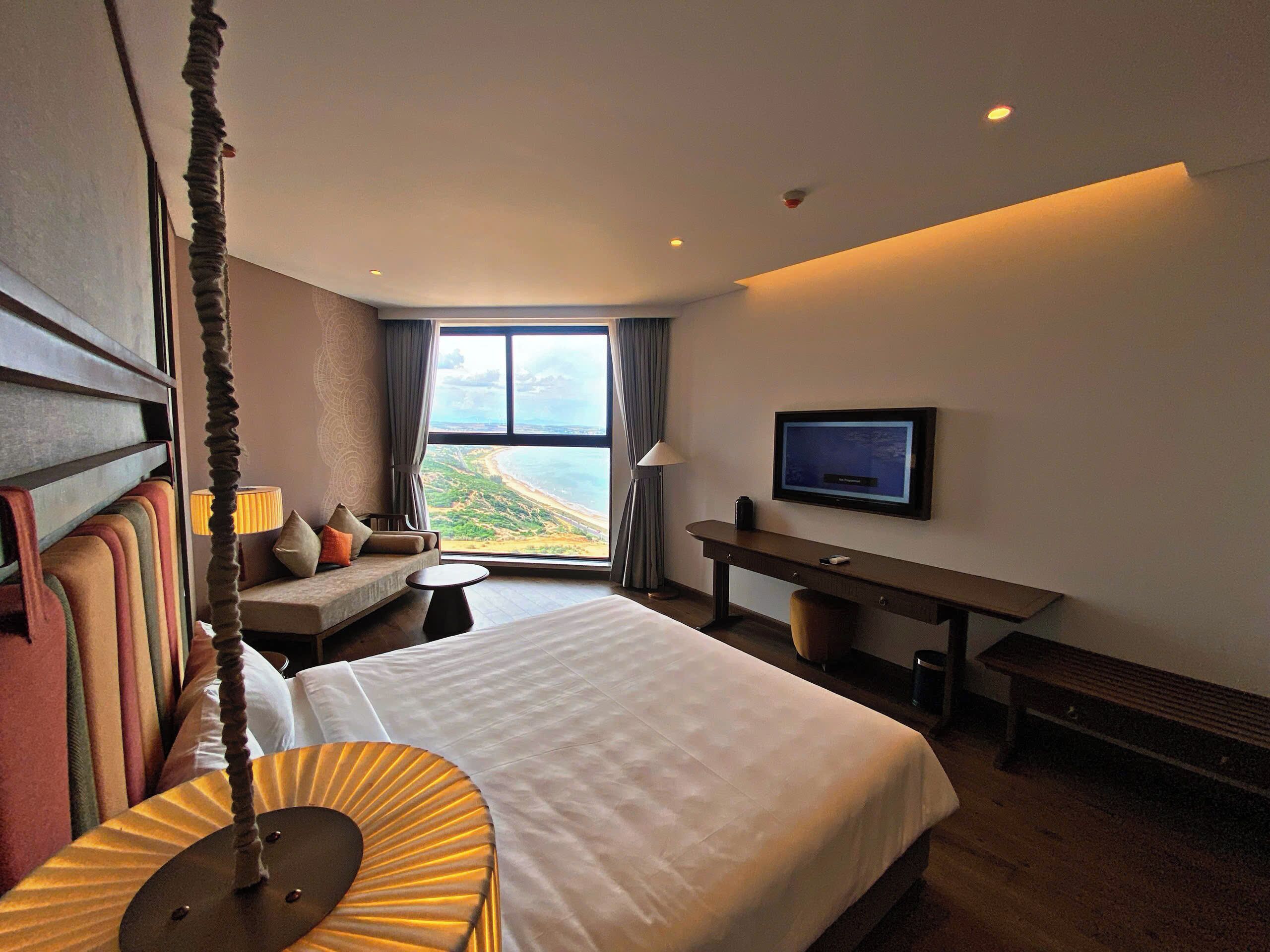 Habitación de hotel con una cama grande, un escritorio, un televisor y vistas a la playa.