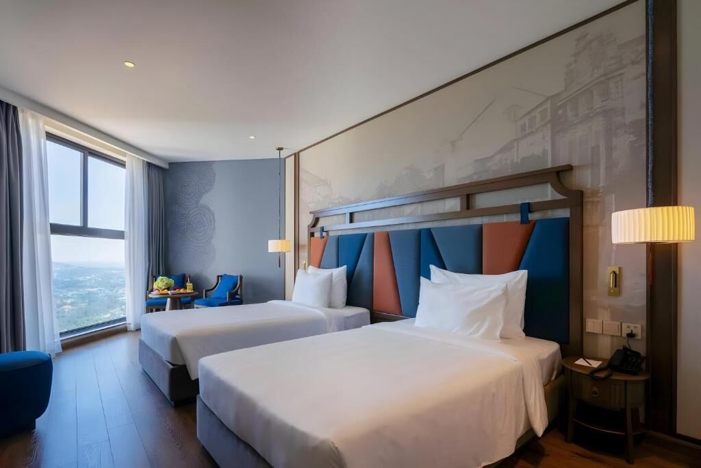 A hotel room with two beds, a view of the city, and a desk with a chair.