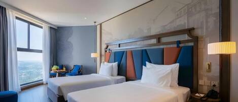 A hotel room with two beds, a view of the city, and a desk with a chair.