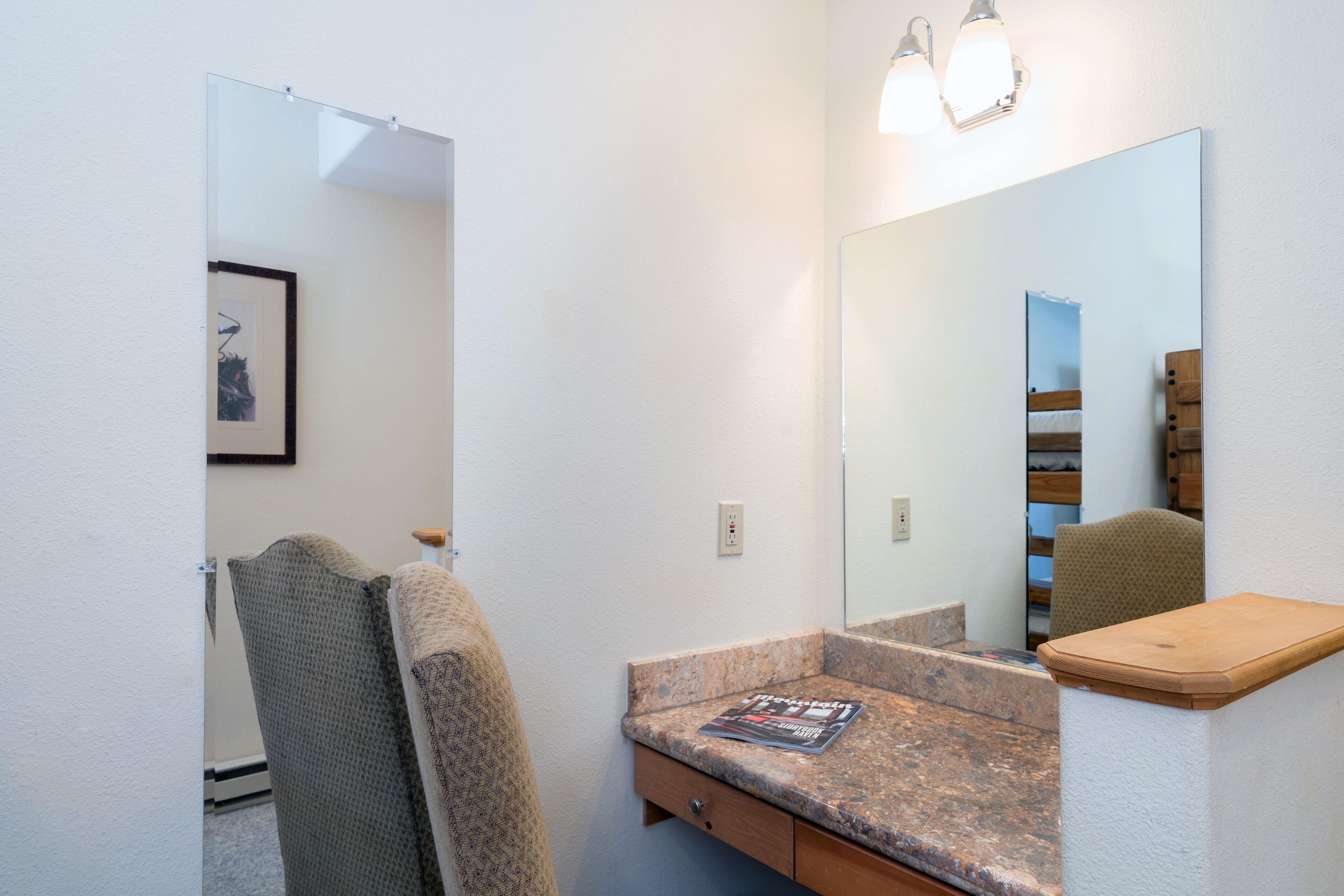 A bathroom with a granite countertop, a wooden vanity, a large mirror, and a towel rack.