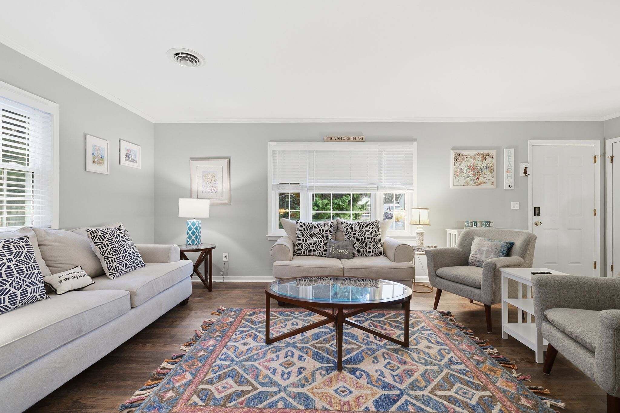 A living room with a beige sofa, a round glass coffee table, and patterned rugs.