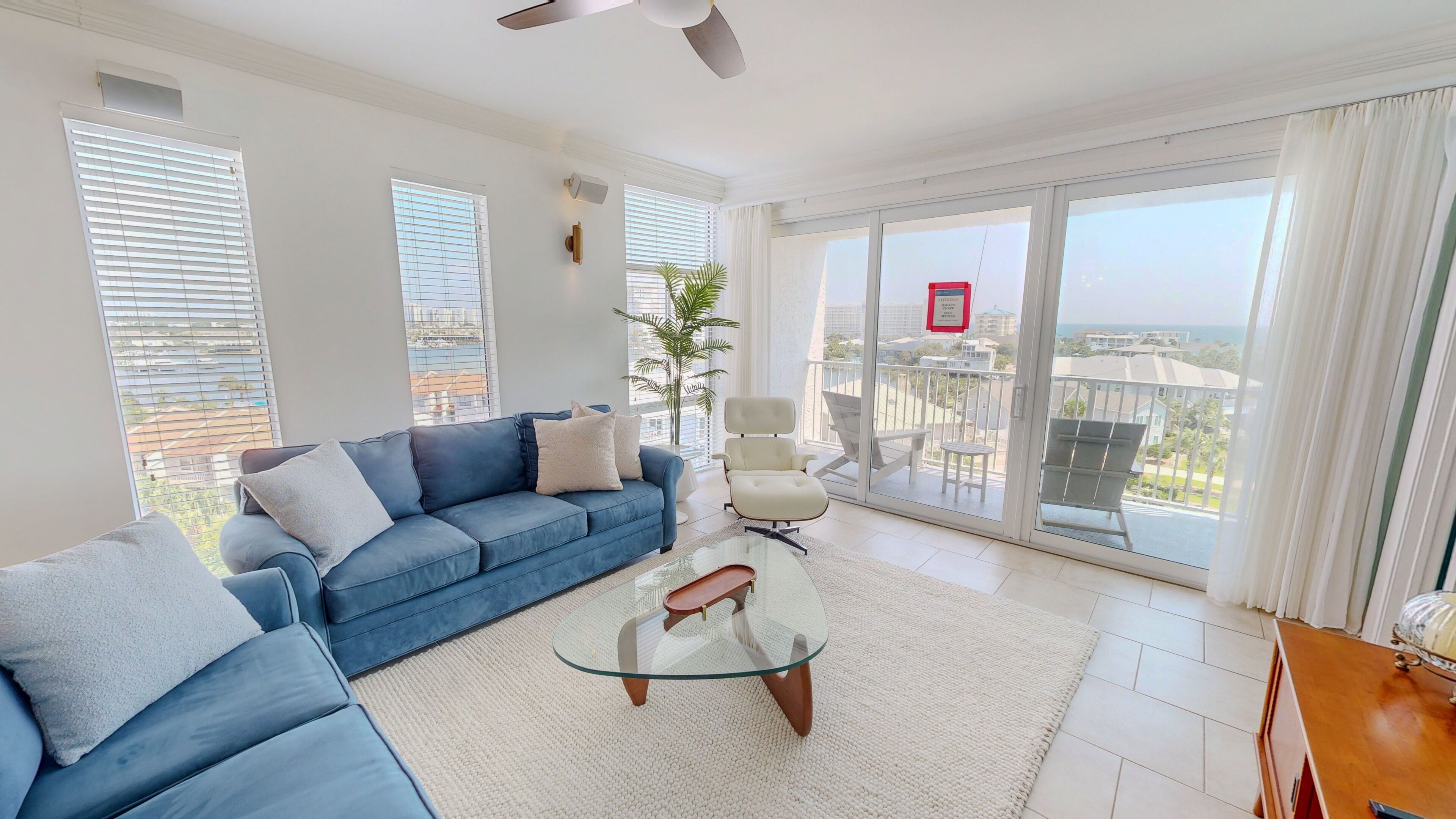 A modern living room with a blue sofa, a glass coffee table, and a view of the city through large windows.