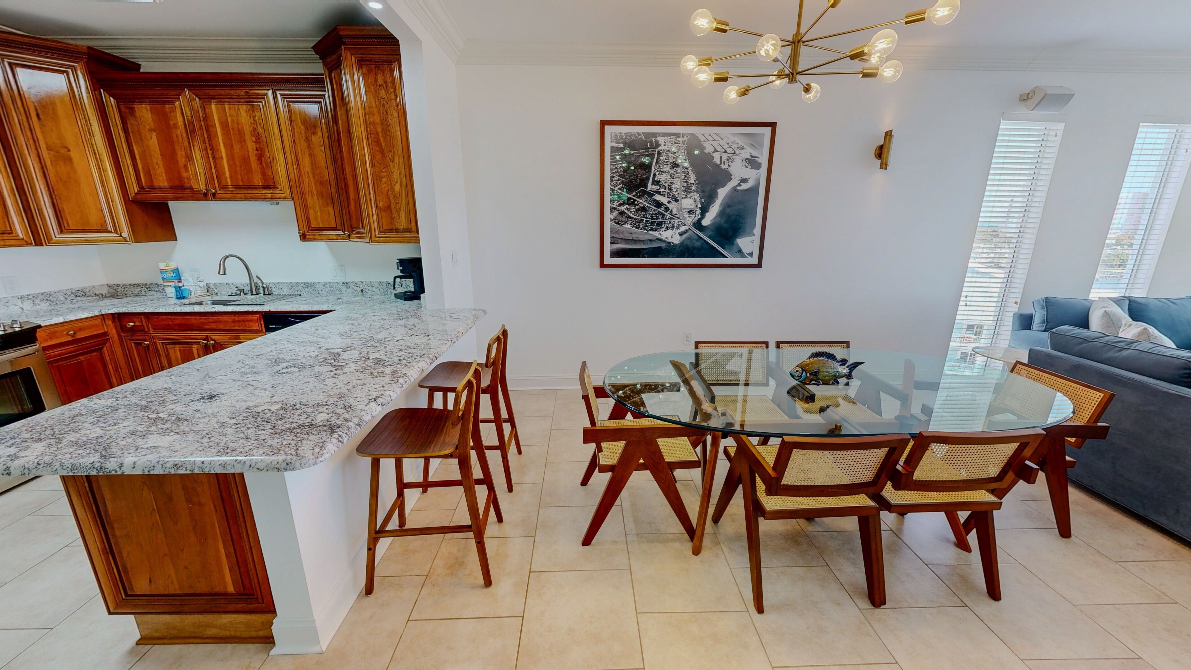 A modern kitchen with wooden cabinets, a marble countertop, and a dining area with a glass table and wooden chairs.