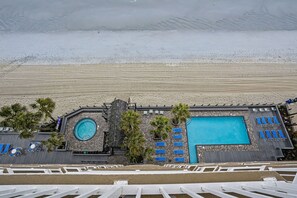 A rooftop pool area with a large pool, lounge chairs, and palm trees. - 1008 Waters Edge Resort 1 Bedroom Condo (Murrells Inlet)